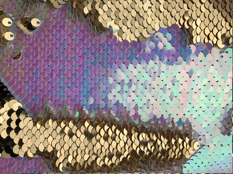 May include: Close-up of iridescent sequins in shades of purple, blue, and gold. The sequins are arranged in a pattern of overlapping scales.