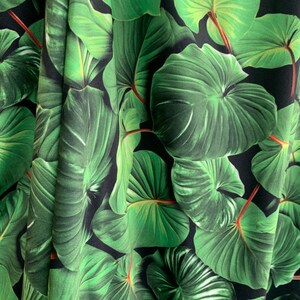 May include: Close-up of a fabric with a green tropical leaf pattern on a black background. The leaves are large and have a realistic texture.