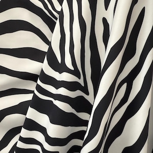 May include: Black and white zebra print fabric with a smooth, silky texture. The fabric is folded in a way that shows the pattern and texture.