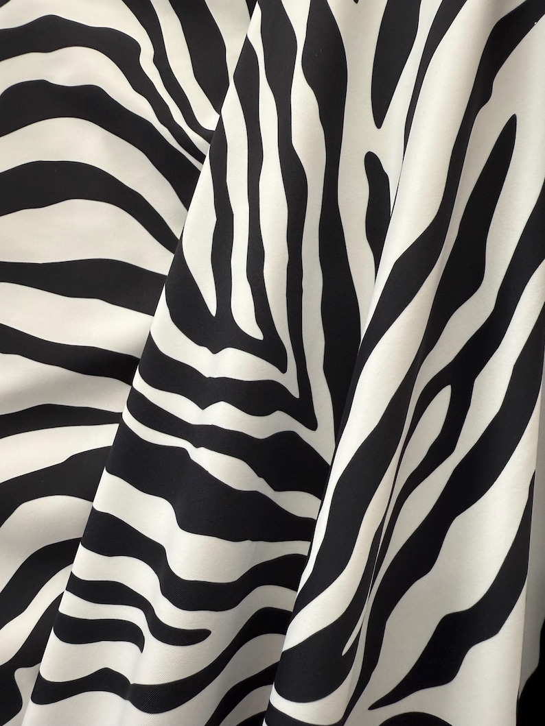 May include: Black and white zebra print fabric with a smooth, silky texture. The fabric is folded in a way that shows the pattern and texture.