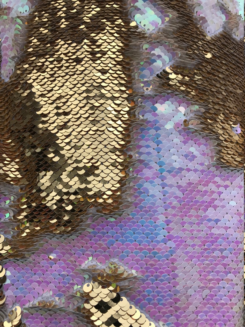 May include: A close-up of iridescent gold and purple sequins arranged in a scale pattern. The sequins are sewn onto a fabric backing.