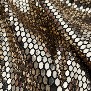 May include: Close-up of a gold and silver fabric with a hexagonal pattern. The fabric is shiny and reflective.