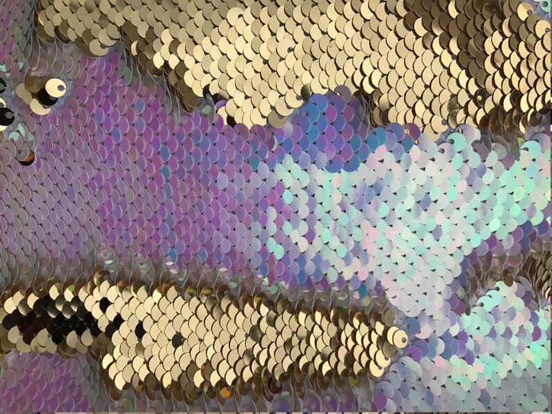 May include: Close-up of iridescent sequins in gold, purple, and blue colours. The sequins are arranged in a pattern of overlapping scales.