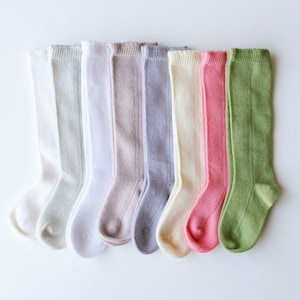 May include: A set of ten knee-high socks in various colors, including white, light green, beige, gray, cream, pink, and green. The socks are made of a soft, knitted fabric and have a delicate lace trim at the top.