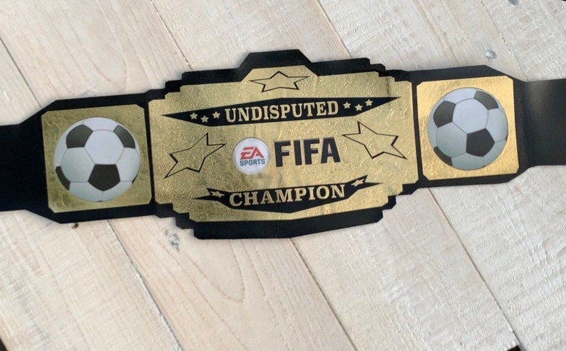 May include: A black and gold championship belt with the words "Undisputed FIFA Champion" and two footballs.