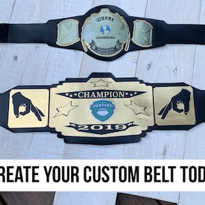 May include: A black championship belt with gold accents and a green and white logo that says "Fantasy" and "2019". The belt has two gold hands on either side of the logo. The text "Champion" is written in gold above the logo.