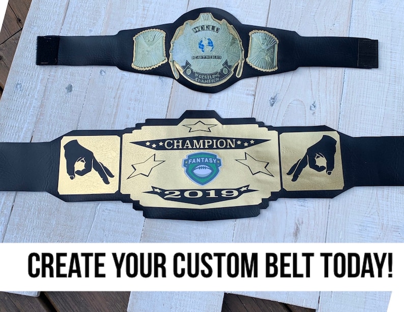 May include: A black championship belt with gold accents and a green and white logo that says "Fantasy" and "2019". The belt has two gold hands on either side of the logo. The text "Champion" is written in gold above the logo.