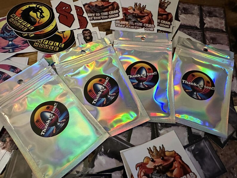 May include: Four iridescent holographic bags with a circular sticker on each. The stickers feature a cartoon illustration of a creature with the text "Thanks a ton!!" printed on each.
