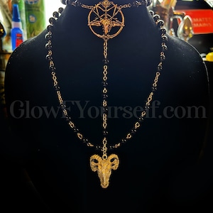 Op de afbeelding: Een zwarte kralenketting met een gouden hanger met een geitenkop in een pentagram. De ketting is gelaagd met een tweede ketting met een kleinere geitenkop-hanger.