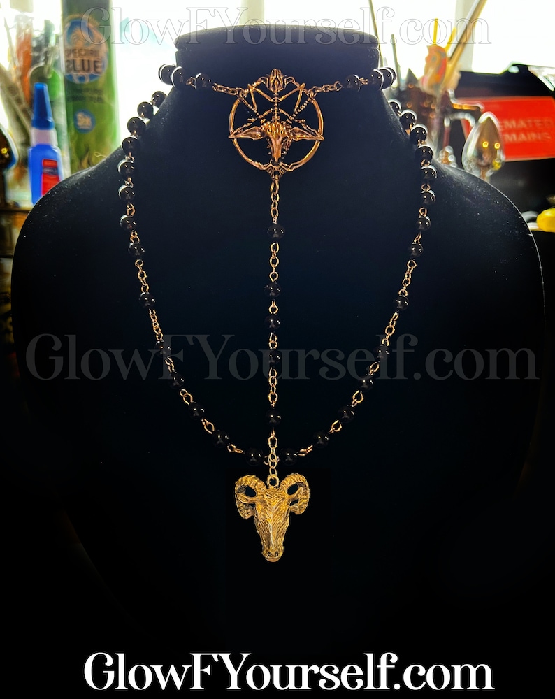 Op de afbeelding: Een zwarte kralenketting met een gouden hanger met een geitenkop in een pentagram. De ketting is gelaagd met een tweede ketting met een kleinere geitenkop-hanger.