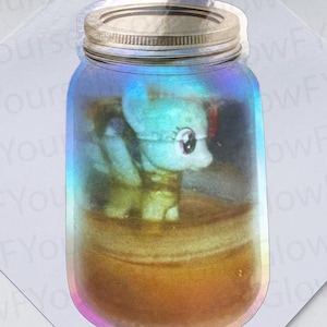 May include: A holographic sticker shaped like a glass mason jar with a metallic lid. Inside the jar is a small, light-colored pony figurine. The sticker has a reflective, iridescent finish that shifts colors, and the background features repeating text.