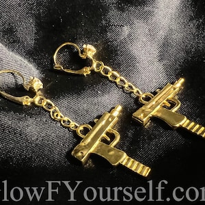 May include: Gold-tone earrings with a dangling chain and a gun charm. The earrings are clip-on style.