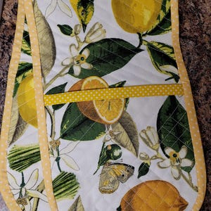 May include: A pair of yellow and white oven mitts with a lemon and butterfly design. The mitts have a yellow trim with white polka dots.