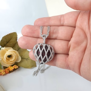 May include: A silver necklace with a heart-shaped pendant. The pendant is made of a delicate silver latticework design and features a red gemstone center.