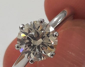 May include: A silver ring with a large, clear, round diamond set in a six-prong setting.