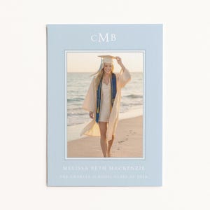 Op de afbeelding: Een lichtblauwe afstudeeraankondiging met een foto van een persoon in een afstudeerjurk en -pet op een strand. De aankondiging heeft de initialen "CMB" bovenaan en de naam "Melissa Beth Mackenzie" en "The Charles School Class of 2026" onderaan.
