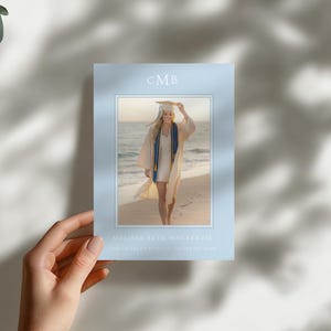 Pu&ograve; includere: Un biglietto di annuncio di laurea con un bordo azzurro, tenuto in mano. Il biglietto presenta una foto di una laureata su una spiaggia. Il testo "CMB" &egrave; in alto, con il nome e la scuola della laureata in basso.