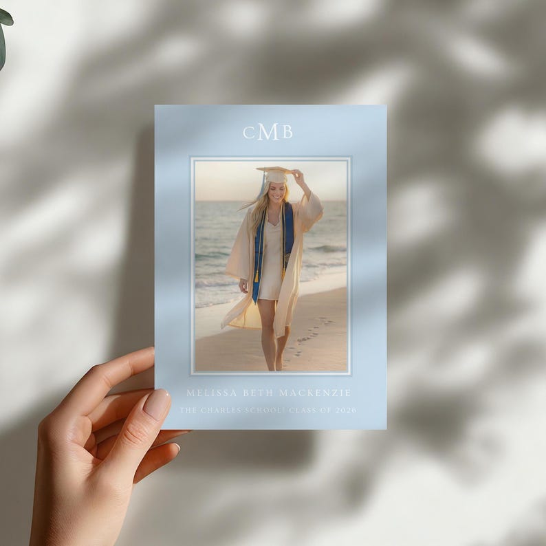 Pu&ograve; includere: Un biglietto di annuncio di laurea con un bordo azzurro, tenuto in mano. Il biglietto presenta una foto di una laureata su una spiaggia. Il testo "CMB" &egrave; in alto, con il nome e la scuola della laureata in basso.