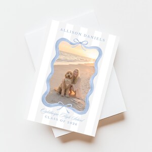 May include: Graduation announcement card with a photo of a person and a dog on a beach. The card has a light blue scalloped border and bows. Text includes "Allison Daniels" and "Oglethorpe High School Class of 2026".