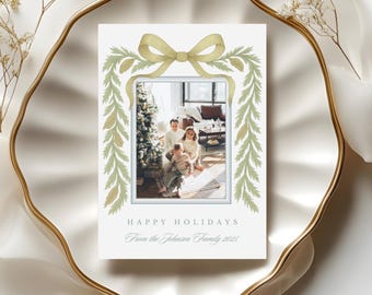 Könnte beinhalten: Eine Weihnachtskarte mit einem Familienfoto in einem weißen Rahmen. Die Karte zeigt ein Aquarelldesign mit einer Schleife und Grünzeug. Der Text lautet "HAPPY HOLIDAYS" und "From the Johnson Family 2025".