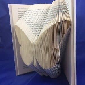 May include: A book folded into the shape of a butterfly. The book is white with black text. The butterfly is standing on a blue surface.