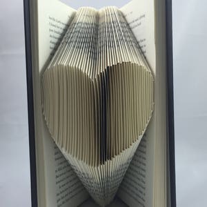 May include: A book with pages folded into the shape of a heart. The book is open and the pages are folded to create a three-dimensional heart shape.