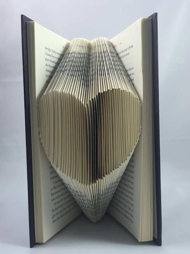 May include: A book with pages folded into the shape of a heart. The book is open and the pages are folded to create a three-dimensional heart shape.