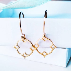 May include: A pair of gold-toned hoop earrings with a geometric quatrefoil design. The earrings are delicate and feature a simple, elegant style.