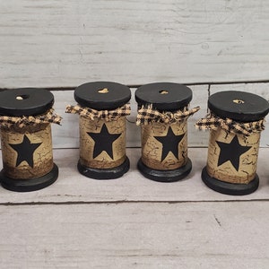 May include: Six black wooden spools with a distressed beige finish and black stars. Each spool is decorated with a black and white gingham ribbon.