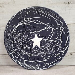 May include: A round, dark blue tray with a white star in the center. The tray has a crackled finish, giving it a distressed look.