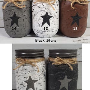 May include: Set of six mason jars with distressed paint and star designs. Three jars have black stars and the numbers 12, 13, and 14. Three jars have gray stars and the numbers 15, 16. Black Stars and Gray Stars.