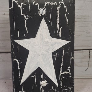 May include: Black and white light switch cover with a white star in the center. The cover has a distressed, crackled paint finish.