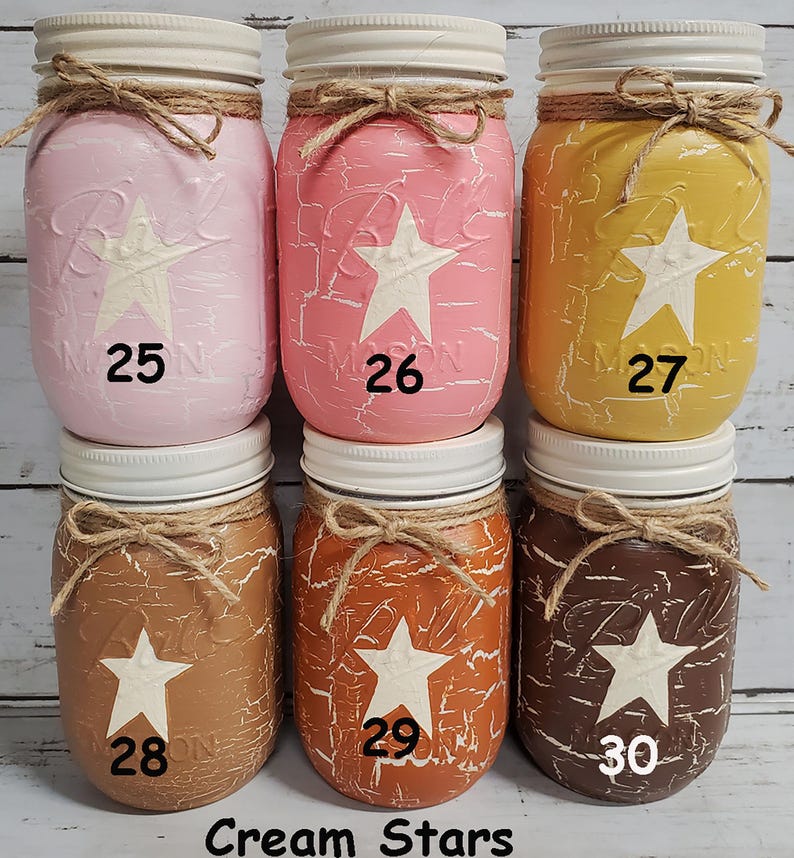May include: Six mason jars with white lids and twine tied around the lids. Each jar is painted with a different color and has a white star painted on the front. The jars are numbered 25 through 30.
