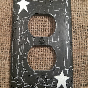 May include: Black and white painted outlet cover with a distressed finish and two white stars. The cover has a double outlet.