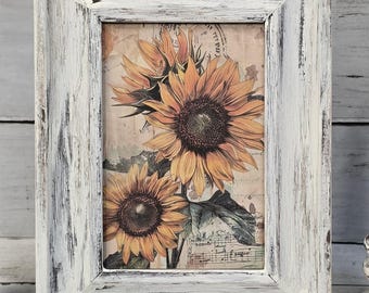 May include: A rectangular framed print featuring three sunflowers in shades of yellow and brown. The print has a vintage aesthetic with musical notes and text in the background. The frame is white with a distressed finish.