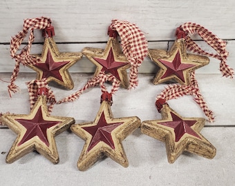 Juego de 6 adornos navideños primitivos en forma de estrella en tonos tostados y burdeos, pintados a mano.