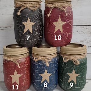 May include: Five mason jars with tan stars painted on them. The jars are painted in different colors: black, red, blue, green. The jars are labeled with numbers 7, 10, 11, 8, and 9. The text "Tan Stars" is at the bottom of the image.