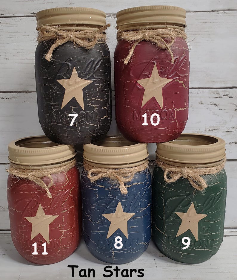 May include: Five mason jars with tan stars painted on them. The jars are painted in different colors: black, red, blue, green. The jars are labeled with numbers 7, 10, 11, 8, and 9. The text "Tan Stars" is at the bottom of the image.