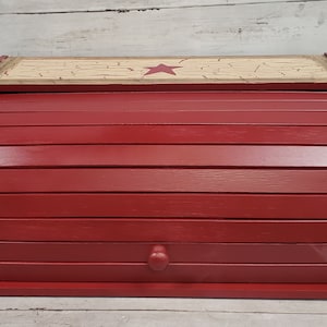May include: Red wooden bread box with a hinged lid and a star design on the top. The lid is made of wood with a distressed finish.
