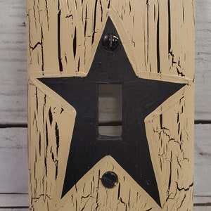 May include: A light beige light switch cover with a black star design. The cover has a distressed, aged look.