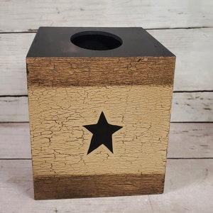 May include: A wooden tissue box cover with a distressed paint finish. The box is painted in shades of brown and beige with a black star in the center.