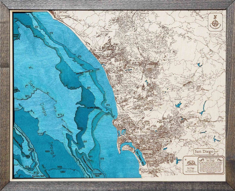 K&ouml;nnte beinhalten: Eine Holzkarte von San Diego, Kalifornien, mit einem blauen und braunen Farbschema. Die Karte zeigt die K&uuml;ste, die Stadt und die Umgebung. Die Karte ist in einem dunklen Holzrahmen gerahmt. Der Text "San Diego" ist in der unteren rechten Ecke der Karte gedruckt.