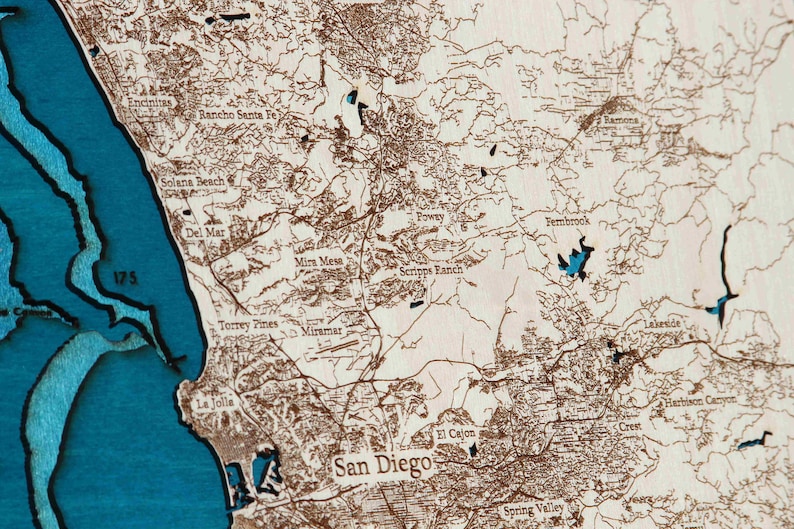 K&ouml;nnte beinhalten: Eine Holzkarte von San Diego, Kalifornien, mit den Stadtvierteln und der Umgebung in Braun umrandet. Die Karte ist auf einem blauen Hintergrund montiert, wobei das Meer und die umliegenden Wasserwege in Blau hervorgehoben sind.