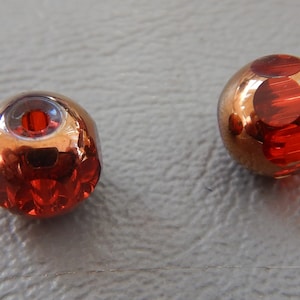 May include: Two round, red and copper glass beads with a shiny, reflective surface. The beads have a faceted design and are perfect for jewelry making.