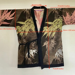 May include: A black kimono-style jacket featuring a bamboo leaf pattern in shades of pink, green, and white. The garment has a solid black trim, wide sleeves, and a tie closure. Measurements include a 28-inch length and 22.5-inch sleeve length.