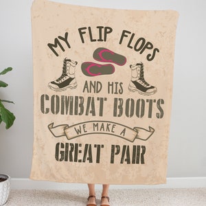 Op de afbeelding: Een beige deken met de tekst "My flip flops and his combat boots we make a great pair" in zwarte en bruine letters. De tekst wordt omringd door een bruin lint. Er zijn illustraties van slippers en laarzen in zwart en wit.