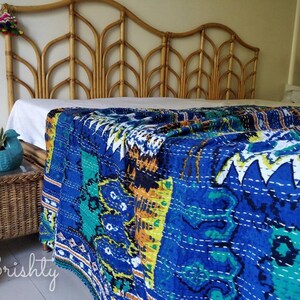 May include: A blue and green kantha quilt with a white background and intricate stitching. The quilt is draped over a bed with a wooden headboard.