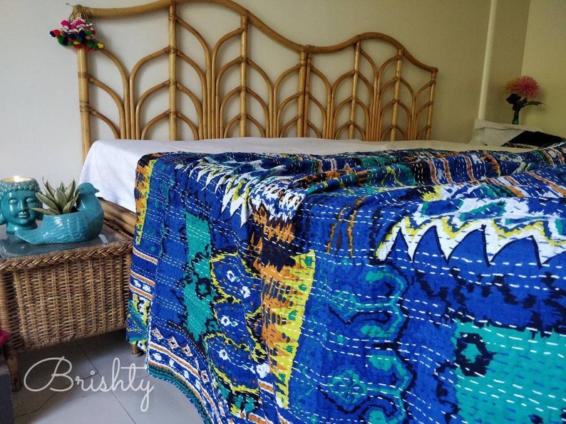 May include: A blue and green kantha quilt with a white background and intricate stitching. The quilt is draped over a bed with a wooden headboard.