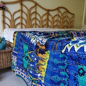 May include: A blue and green kantha quilt with a white background and intricate stitching. The quilt is draped over a bed with a bamboo headboard.
