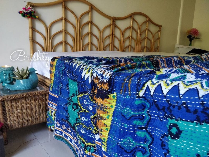 May include: A blue and green kantha quilt with a white background and intricate stitching. The quilt is draped over a bed with a bamboo headboard.
